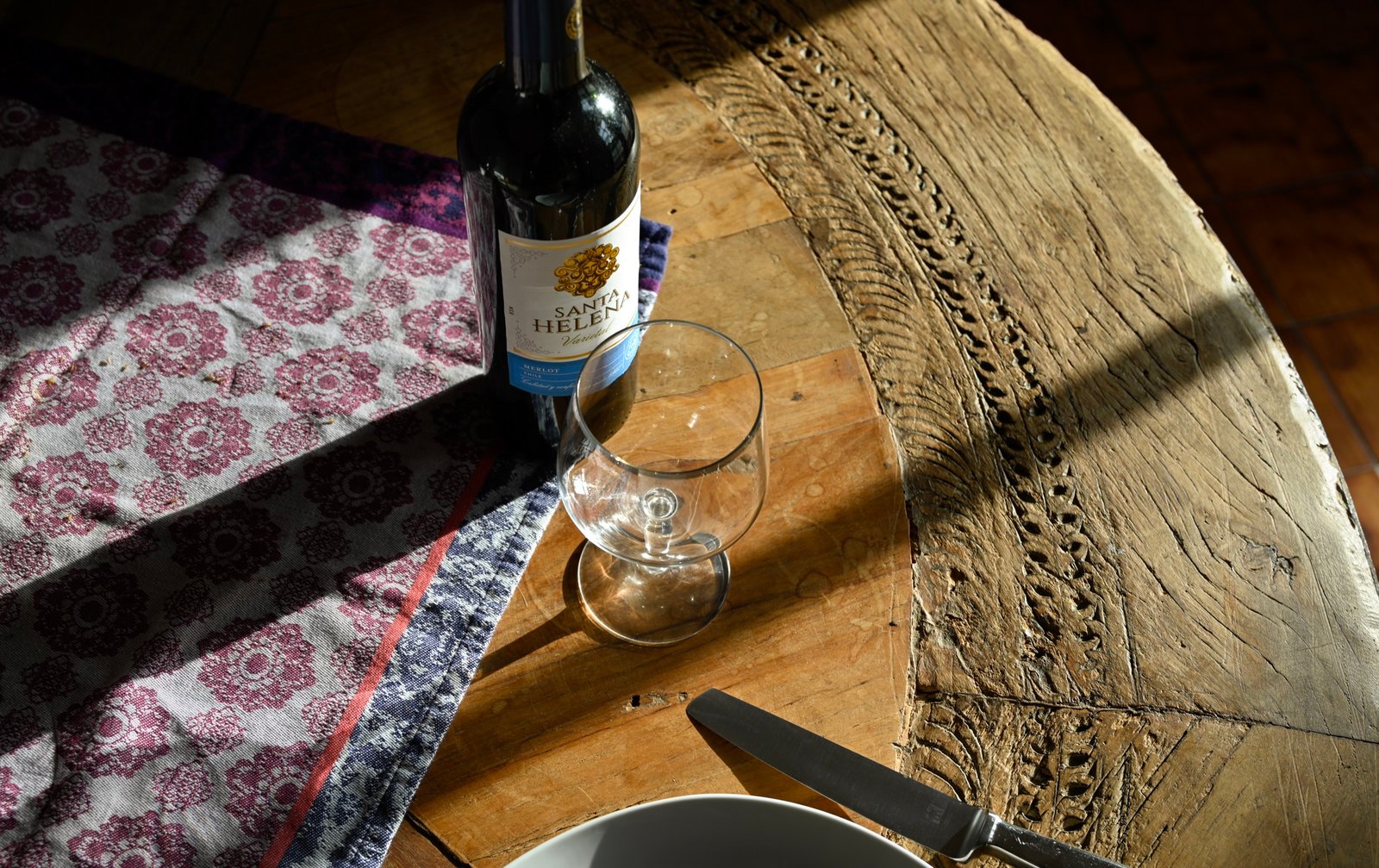 Afternoon light falling across wine and a place setting on an old wooden table
